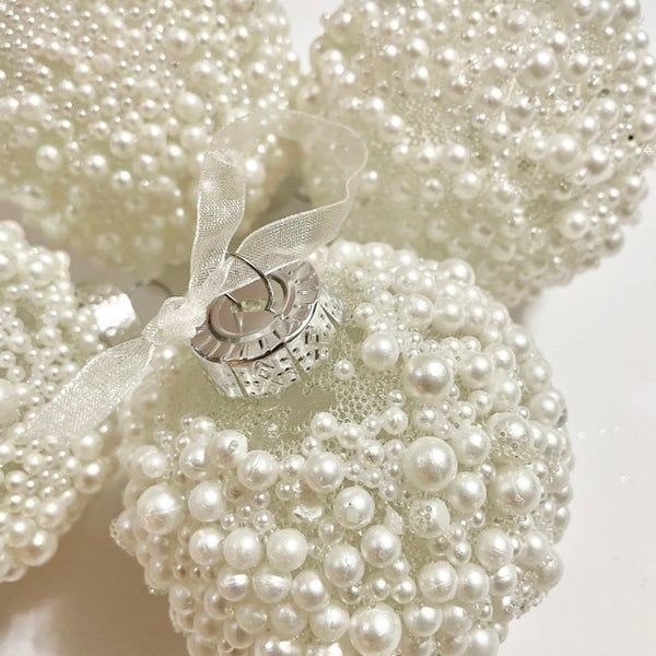 Close-up of ivory pearl-covered Christmas ornaments tied with a white satin ribbon