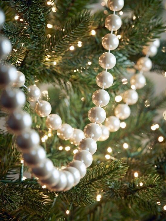 Faux pearl bead garland draped over a green Christmas tree with warm white lights