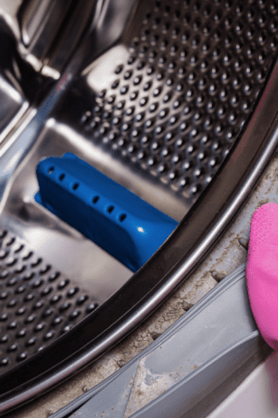 Black mold and grime buildup inside front-load washing machine rubber door seal during cleaning.