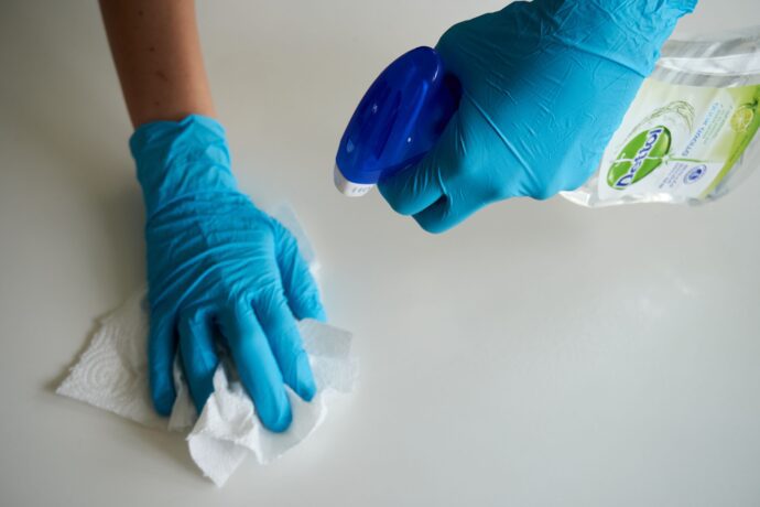 Hands wearing blue gloves cleaning a surface with disinfectant spray