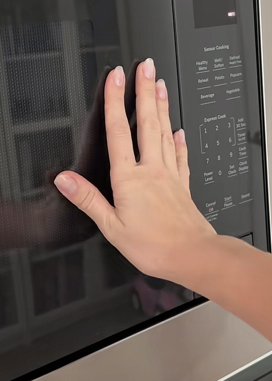 Hand pressed on a black microwave door to test for fingerprints after cleaning